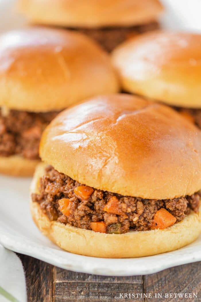 A Sloppy Joe sitting on a white plate with a few more in the background.