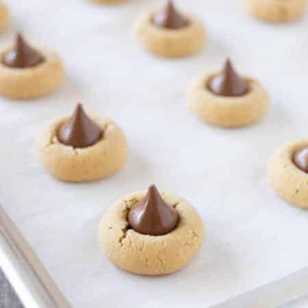 Peanut butter kiss cookies sitting on a lined baking sheet.