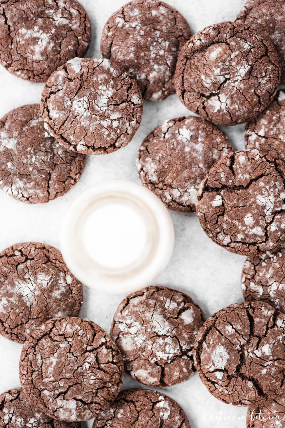 Chocolate crinkle cookies laying on parchment paper with a jar of milk next to them.