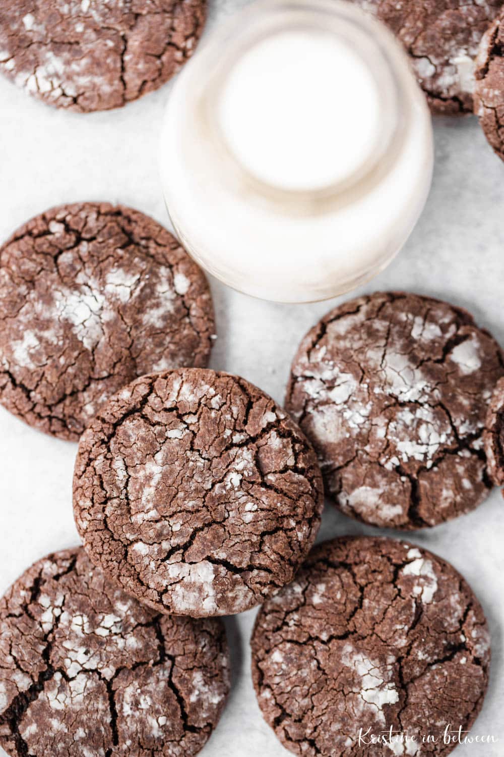 Chocolate cookies laying on parchment paper with a small jar of milk.