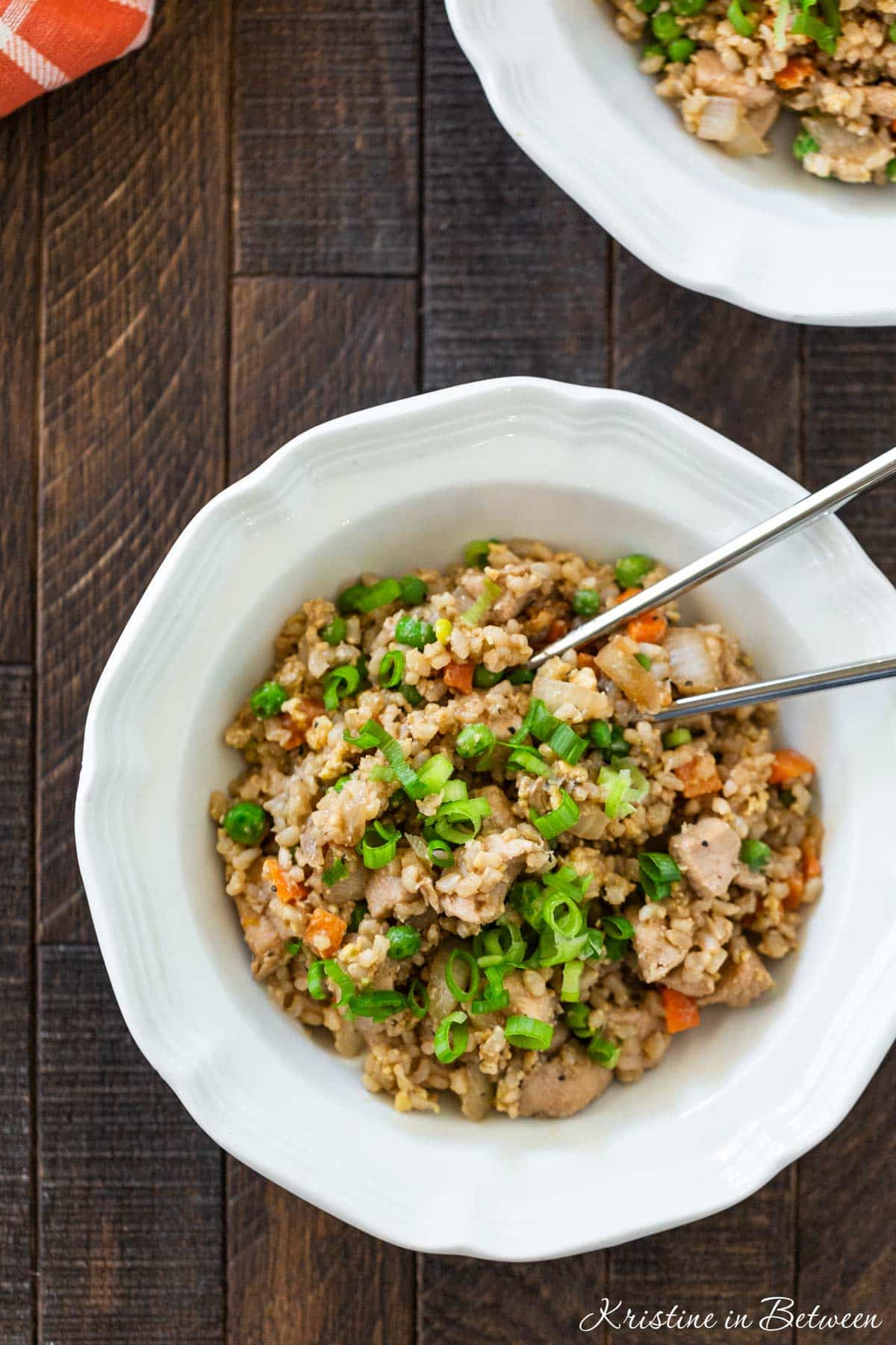 Two bowls of chicken fried rice with sliced green onions sprinkled on top.