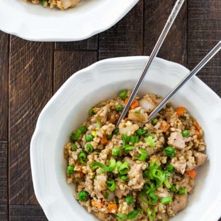 Two bowls of chicken fried rice with sliced green onions sprinkled on top.