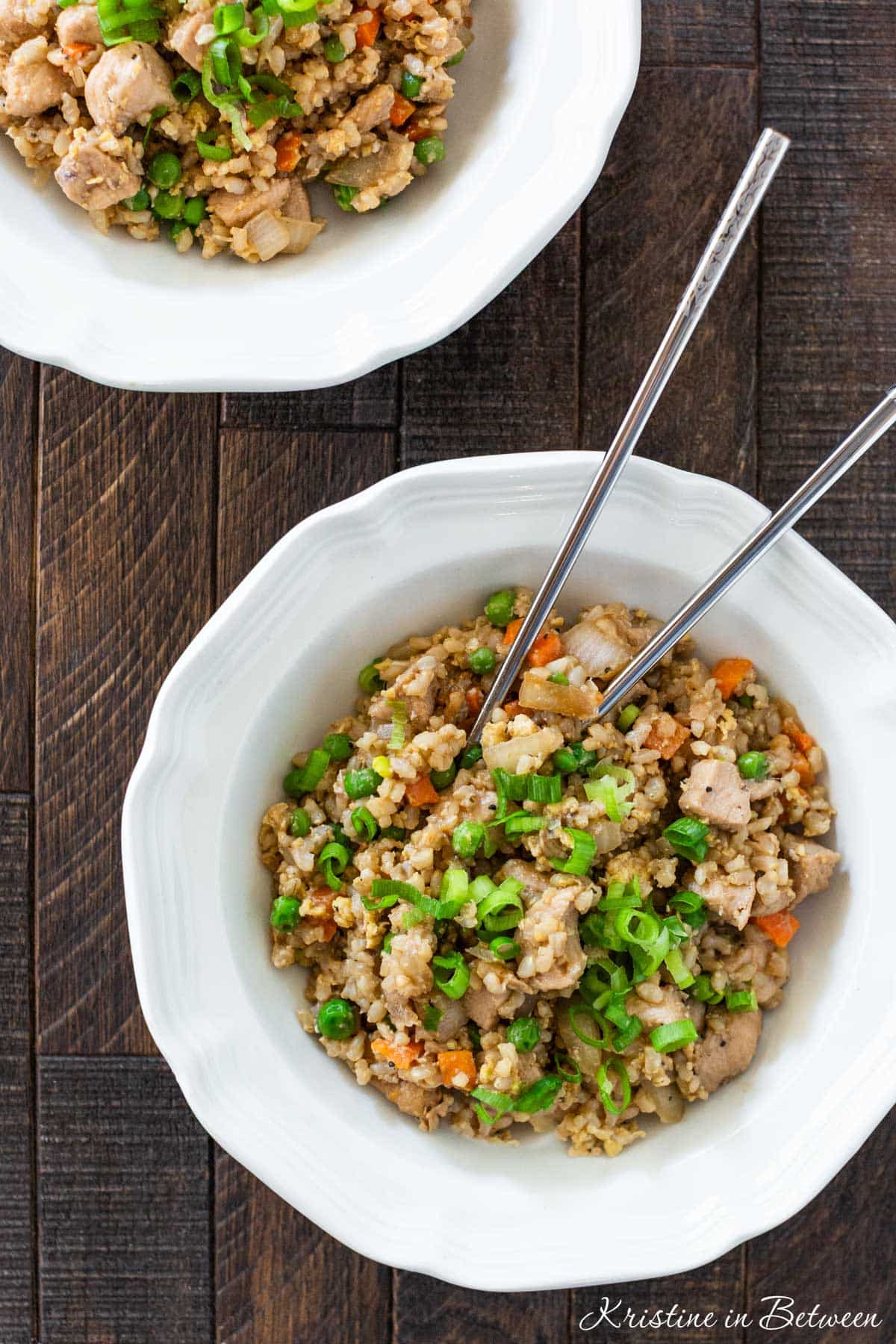 Two bowls of chicken fried rice with sliced green onions sprinkled on top.