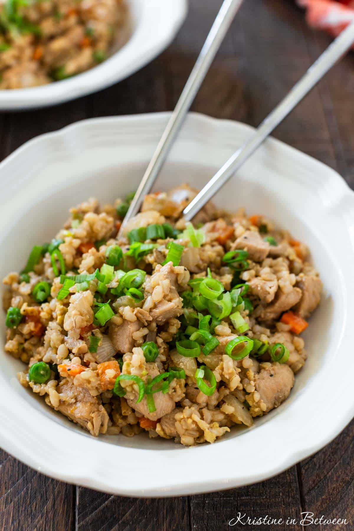 Two bowls of chicken fried rice with sliced green onions sprinkled on top.