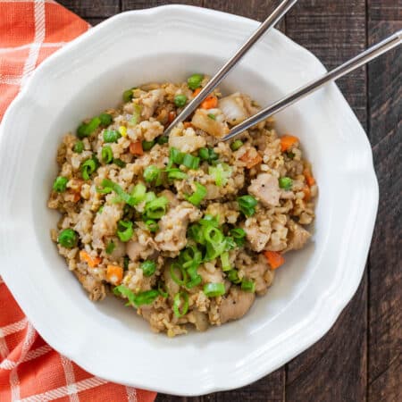 A bowl of chicken fried rice with chopsticks in it.