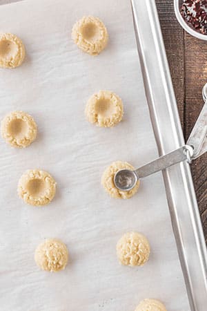 Thumbprint cookies laying on parchment paper with a measuring spoon laying on top.