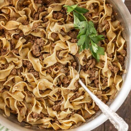 A pan of cooked beef and noodles with a fresh leaf of parsley on top.