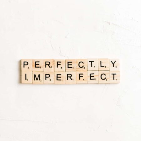 Scrabble tiles laying on a white background spelling out "perfectly imperfect".