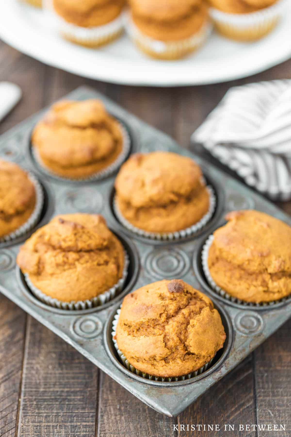 Pumpkin muffins sitting in a muffin tin with a knife and a striped napkin sitting next to them.