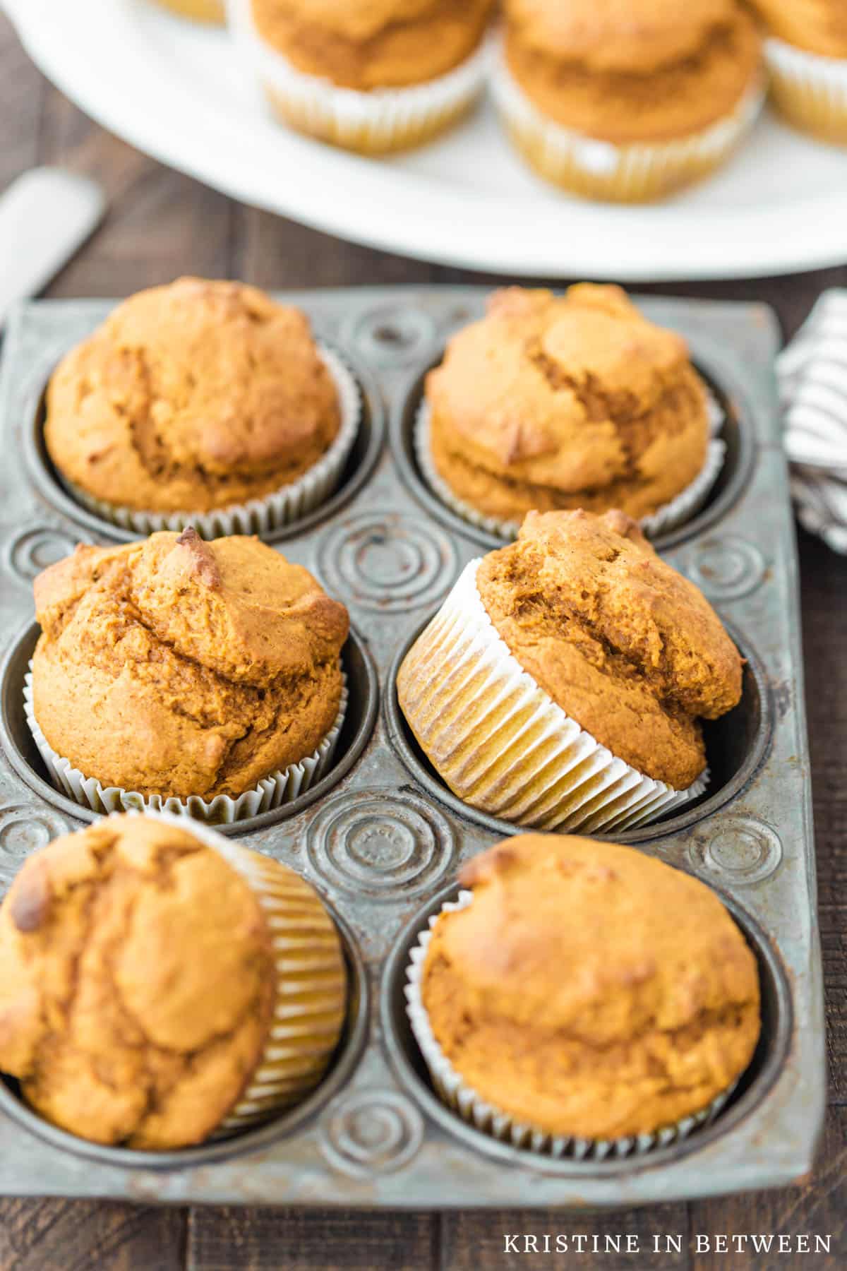 Pumpkin muffins in a muffin tin with one tilted to the side to show detail.