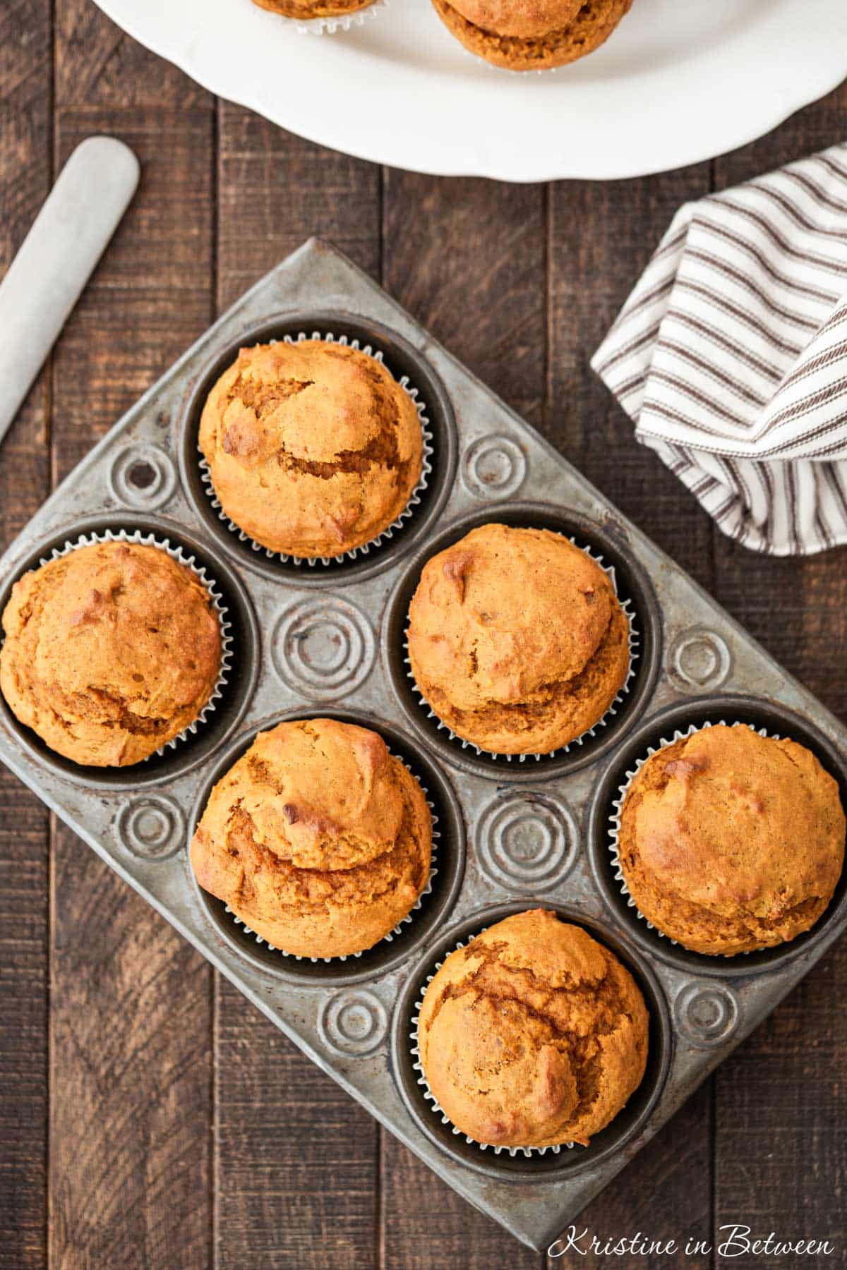 Pumpkin muffins in a muffin tin with a striped napkin and a knife next to them.