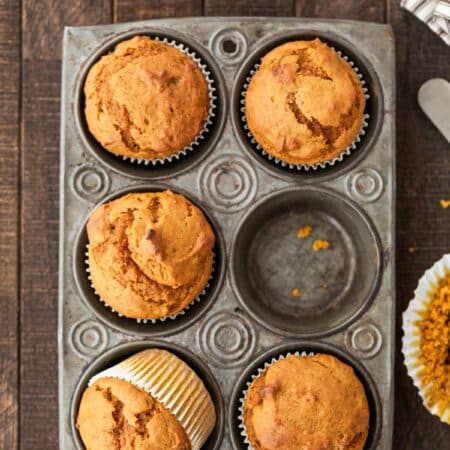 Pumpkin muffins in a muffin tin with a striped napkin and a knife next to them.
