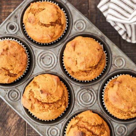 Pumpkin muffins in a muffin tin with a striped napkin and a knife next to them.