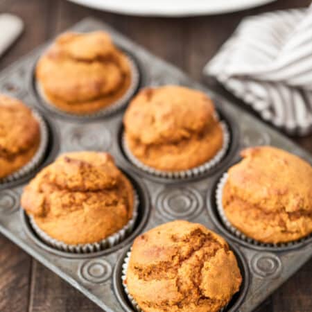 Pumpkin muffins in a muffin tin with a striped napkin and a knife next to them.