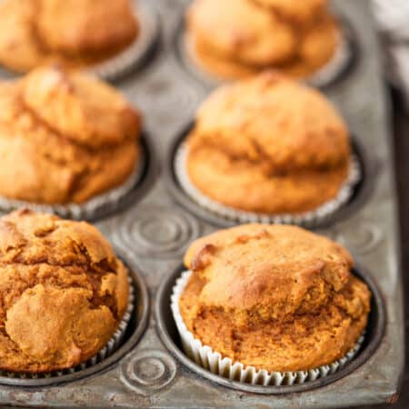 Pumpkin muffins in a muffin tin with a striped napkin and a knife next to them.