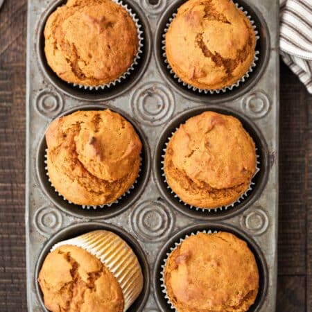Pumpkin muffins in a muffin tin with a striped napkin and a knife next to them.