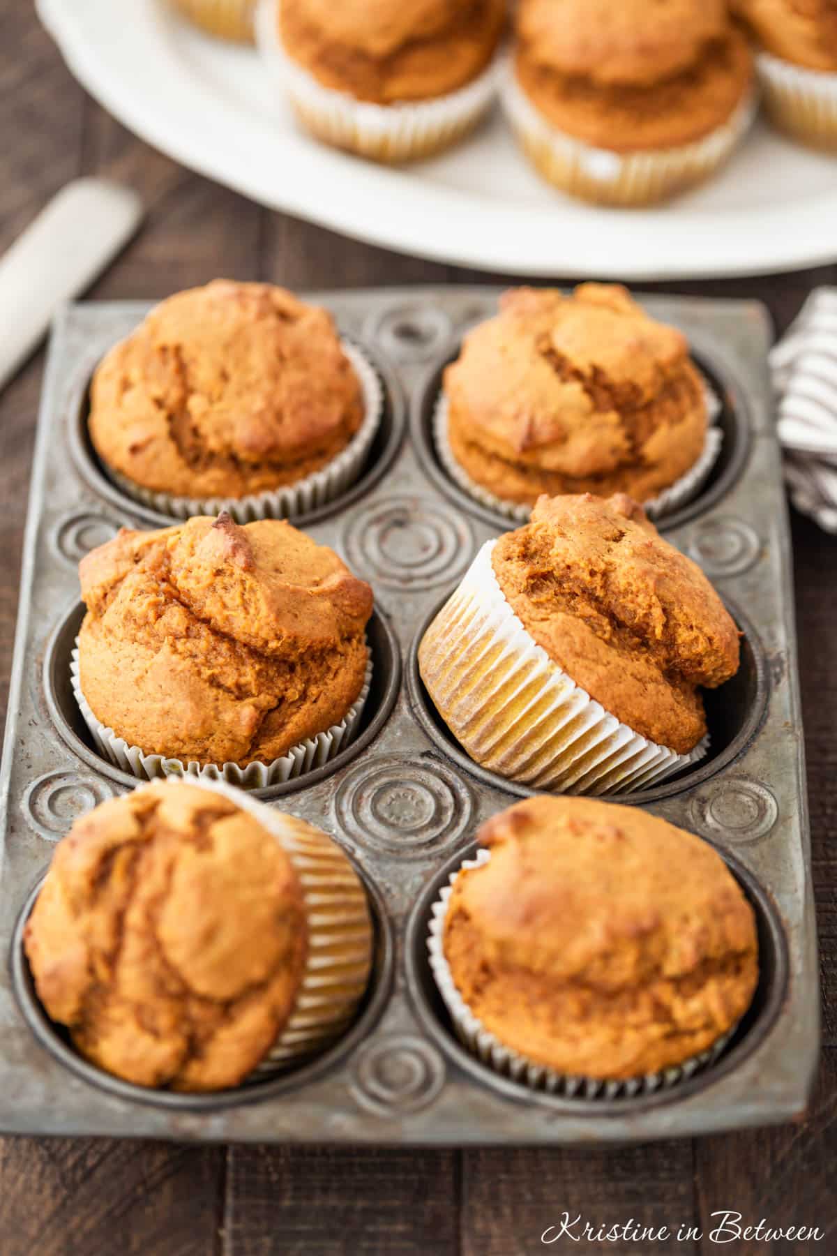 Pumpkin muffins in a muffin tin with a striped napkin and a knife next to them.