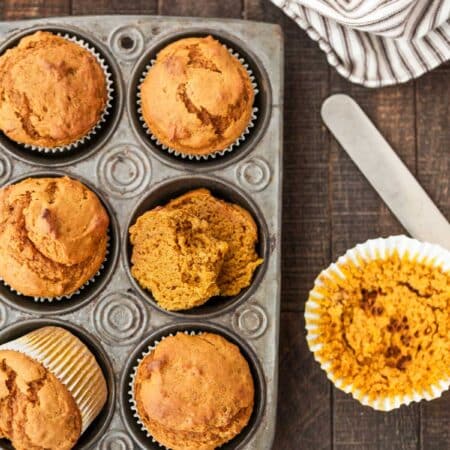 Pumpkin muffins in a muffin tin with a striped napkin and a knife next to them.