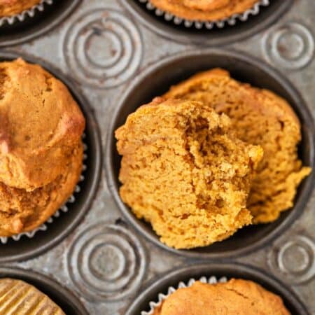Pumpkin muffins in a muffin tin with a striped napkin and a knife next to them.