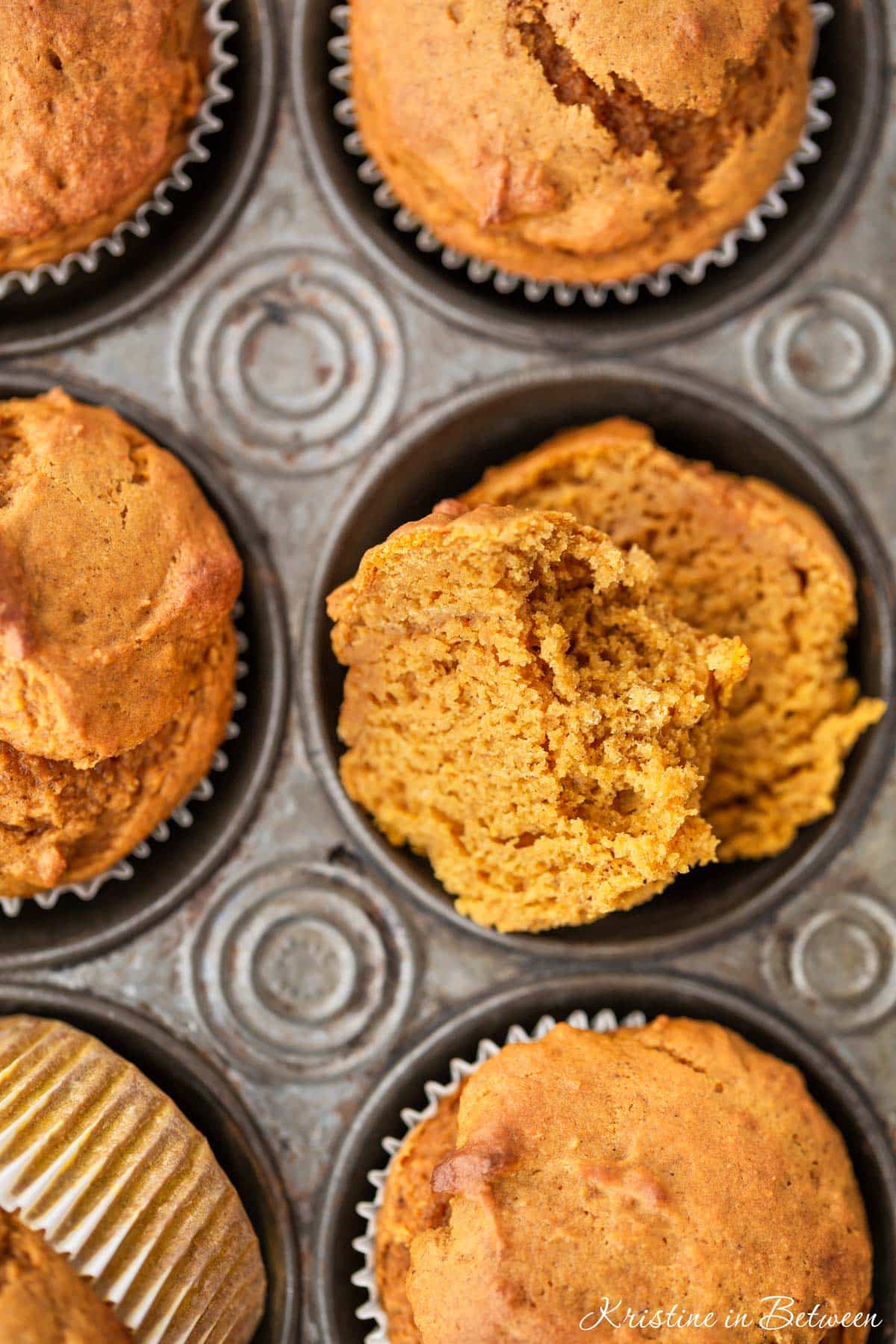 Pumpkin muffins in a muffin tin with a striped napkin and a knife next to them.