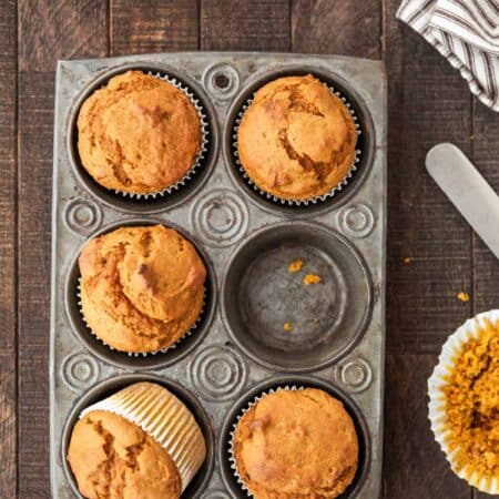 Pumpkin muffins in a muffin tin with a striped napkin and a knife next to them.
