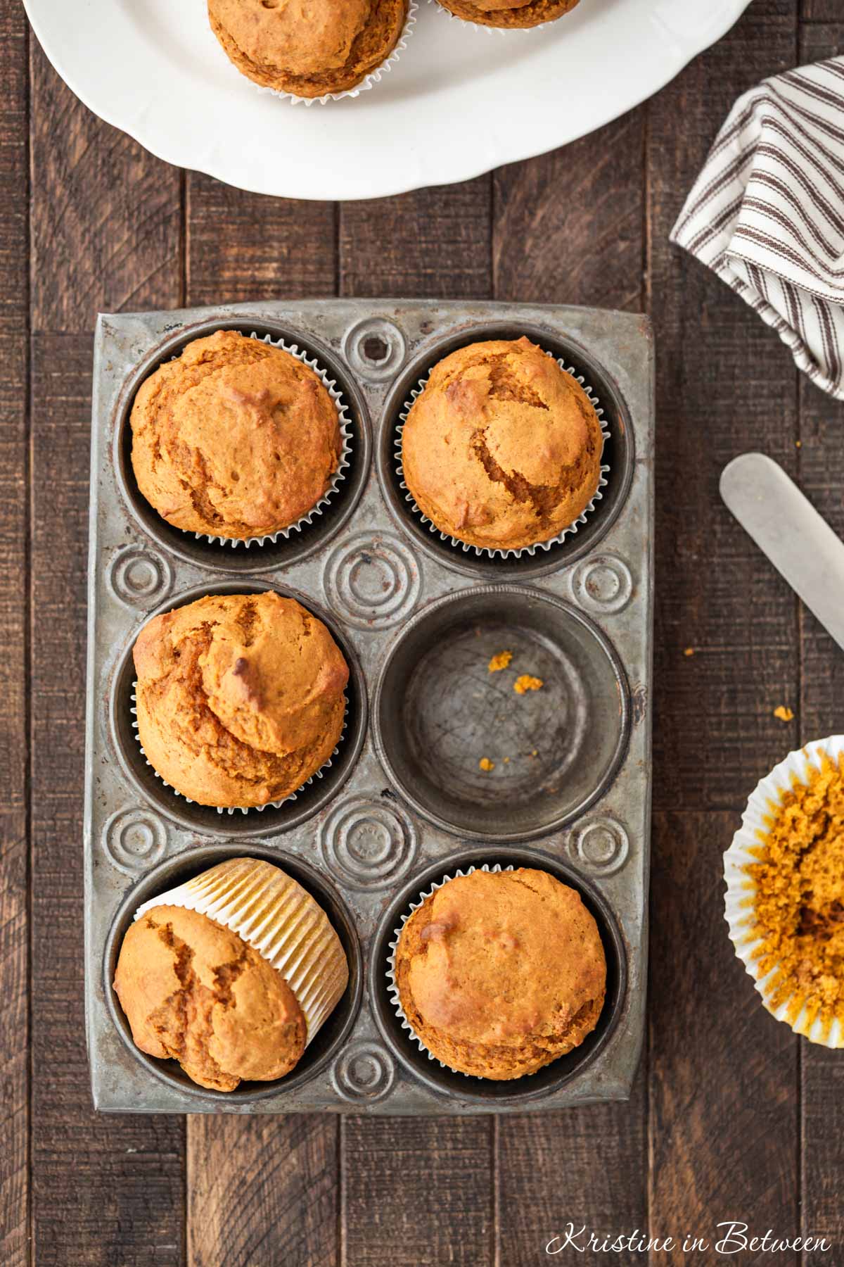 Pumpkin muffins in a muffin tin with a striped napkin and a knife next to them.
