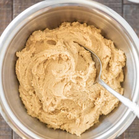 A bowl of peanut butter cookie dough with a cookie scoop and a small bowl of peanut butter sitting next to it.