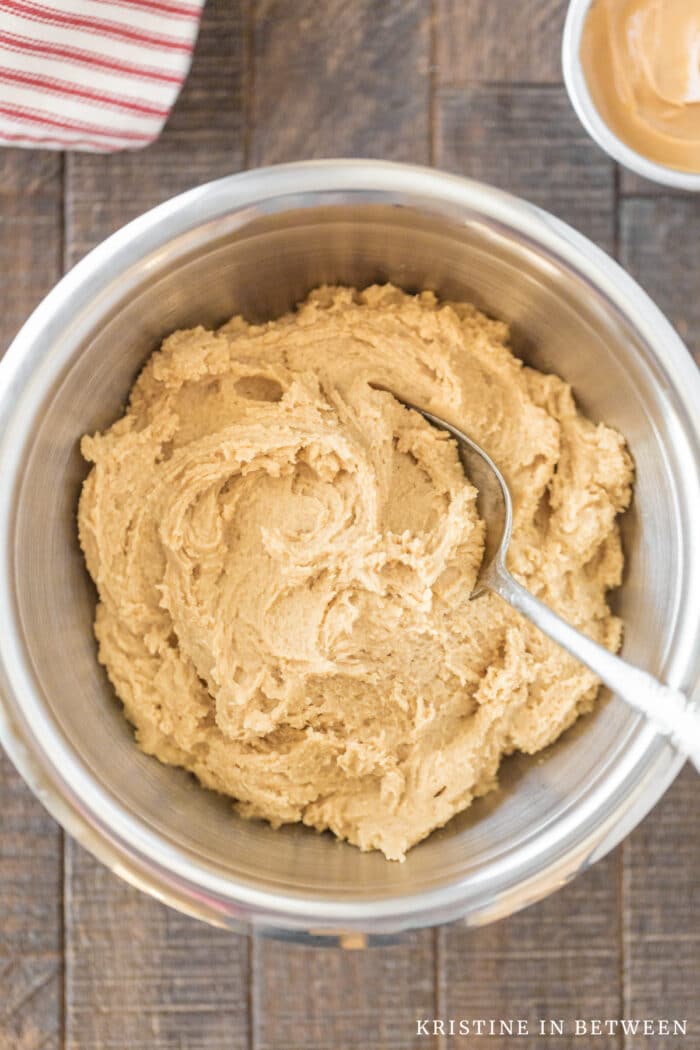 A bowl of peanut butter cookie dough with a cookie scoop and a small bowl of peanut butter sitting next to it.