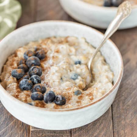 Two bowls of oatmeal topped with blueberries and cinnamon with an orange napkin in the background.