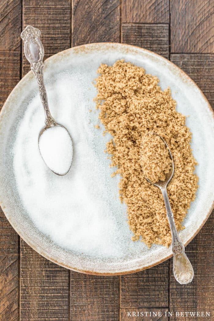 A plate filled with half white sugar and half brown sugar with two antique spoons.