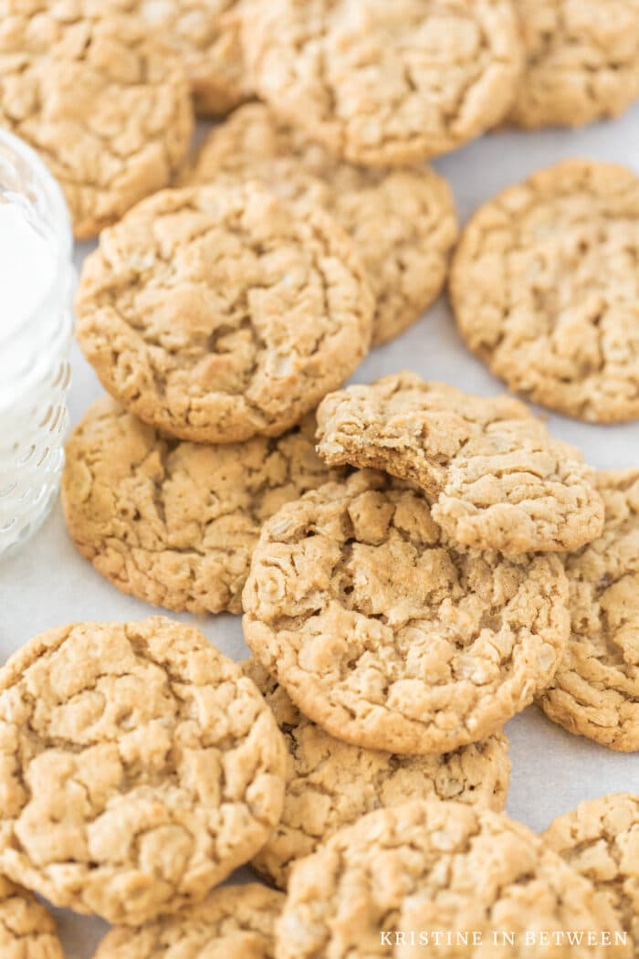 A cookie with a bite out of it laying on top of other cookies with a glass of milk next to them.