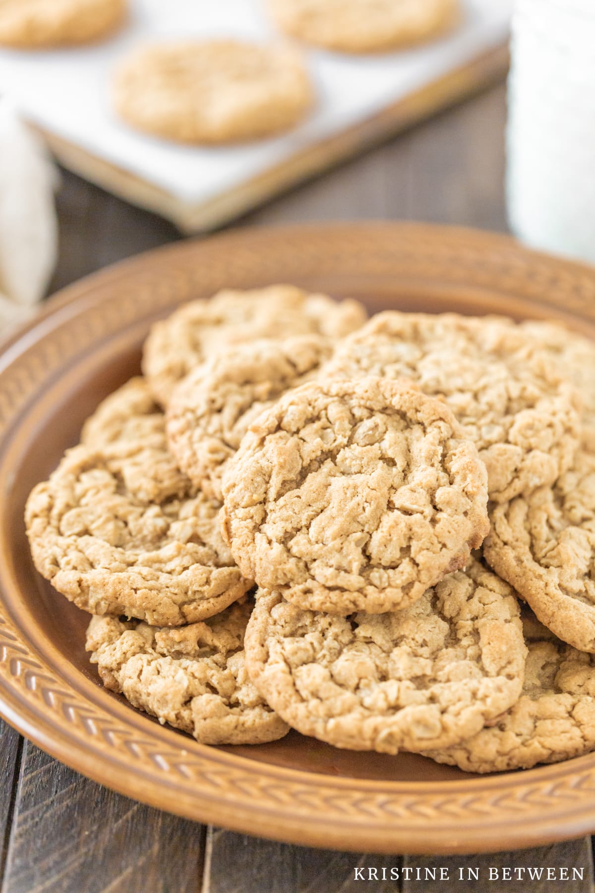 Peanut butter oatmeal cookies sitting on a brown plate with a glass of milk in the background.