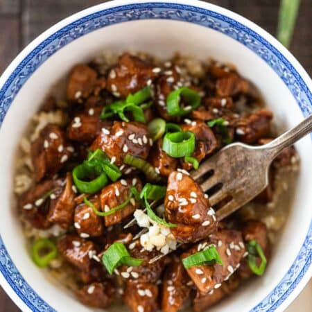 A chicken teriyaki rice bowl with a fork stuck in it and some green onion in the background.