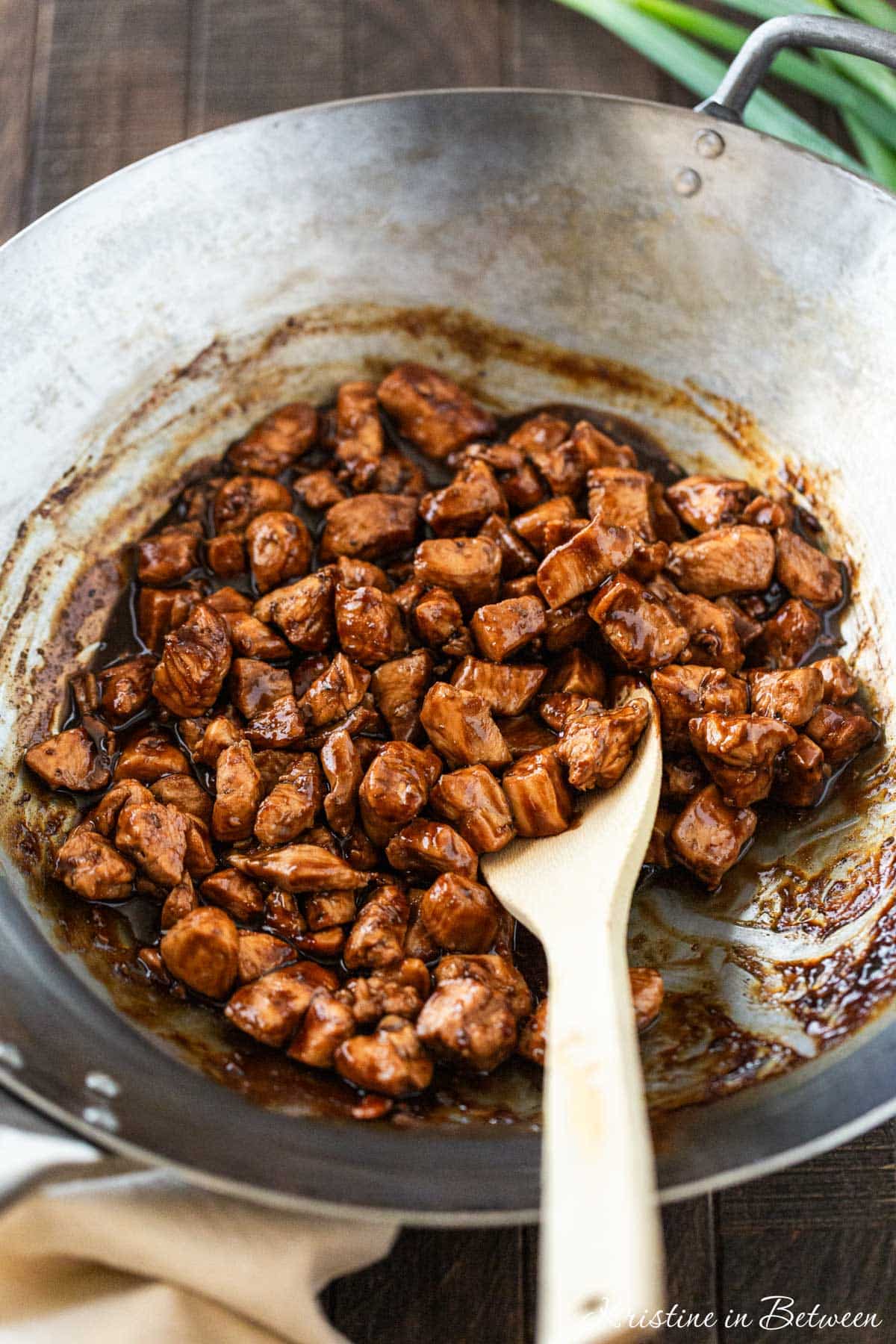 Cooked chicken in teriyaki sauce in a wok pan with a wooden spoon.
