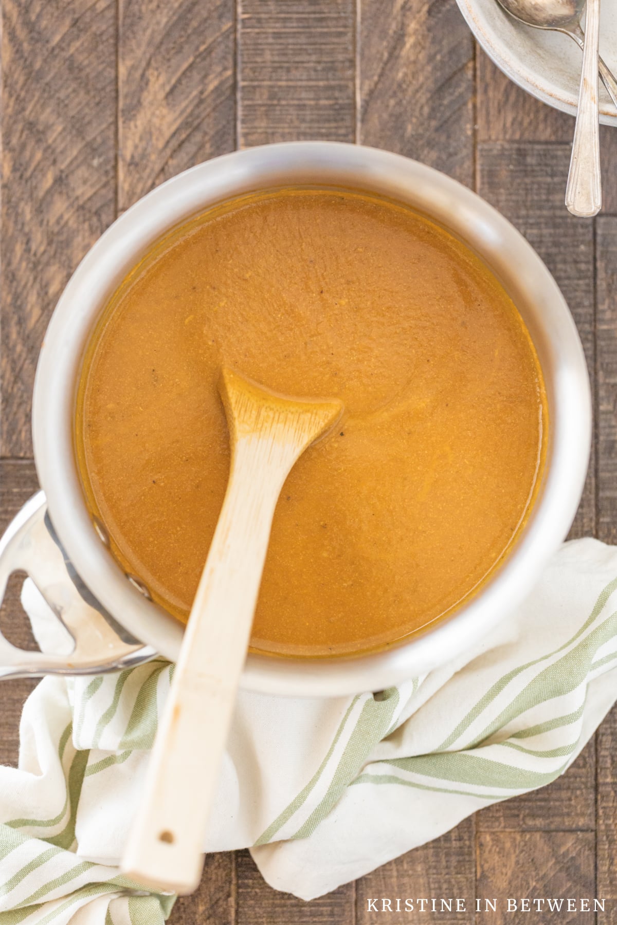 A pot of pumpkin soup sitting with a wooden spoon in it and a green striped napkin next to it.