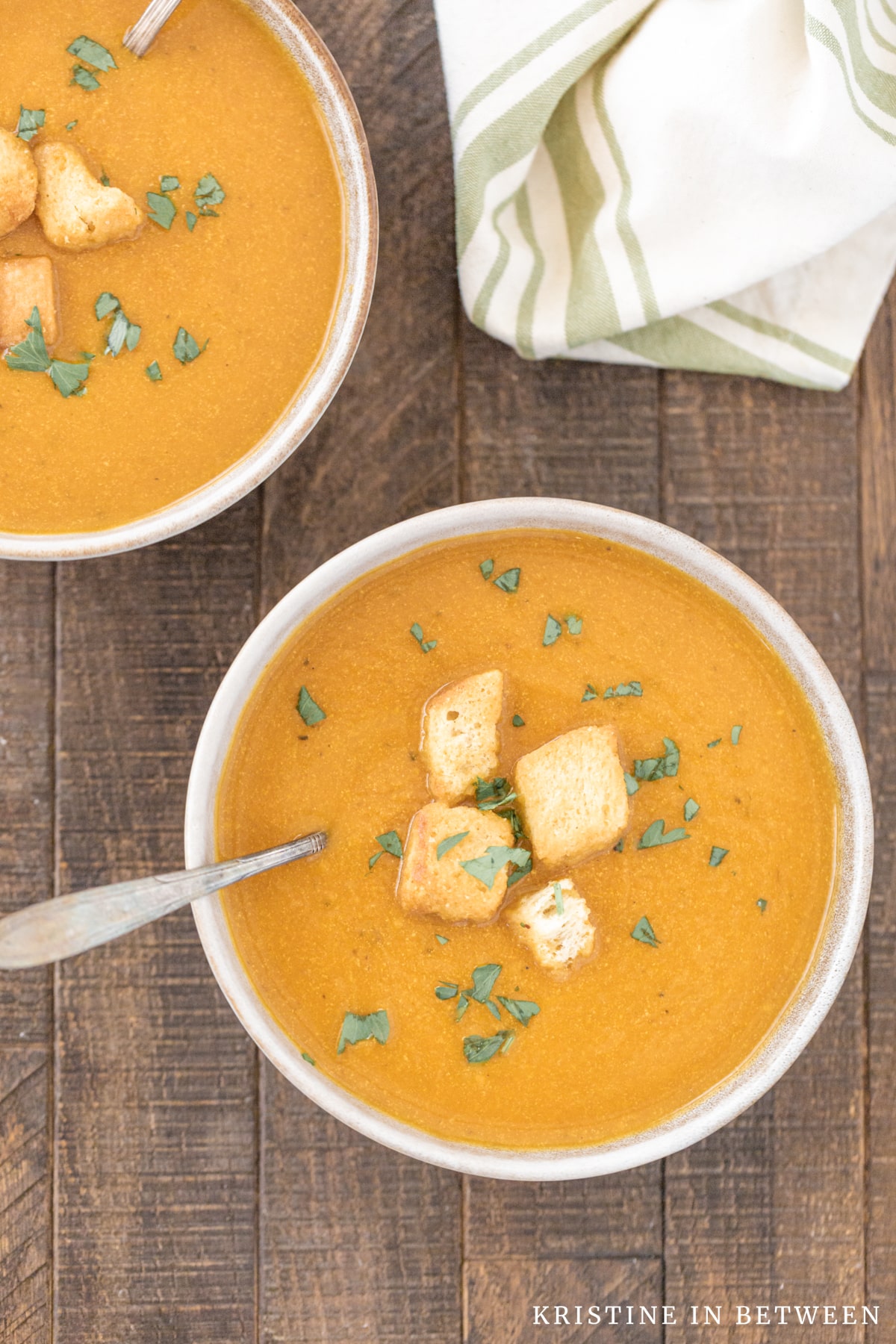 A bowl of pumpkin soup with croutons on top sitting with a spoon in it.