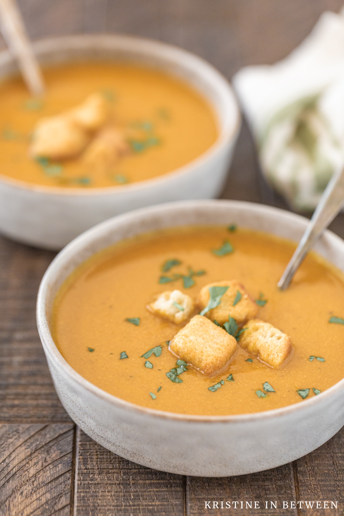 Two bowls of pumpkin soup with croutons on top and spoons in the soup.