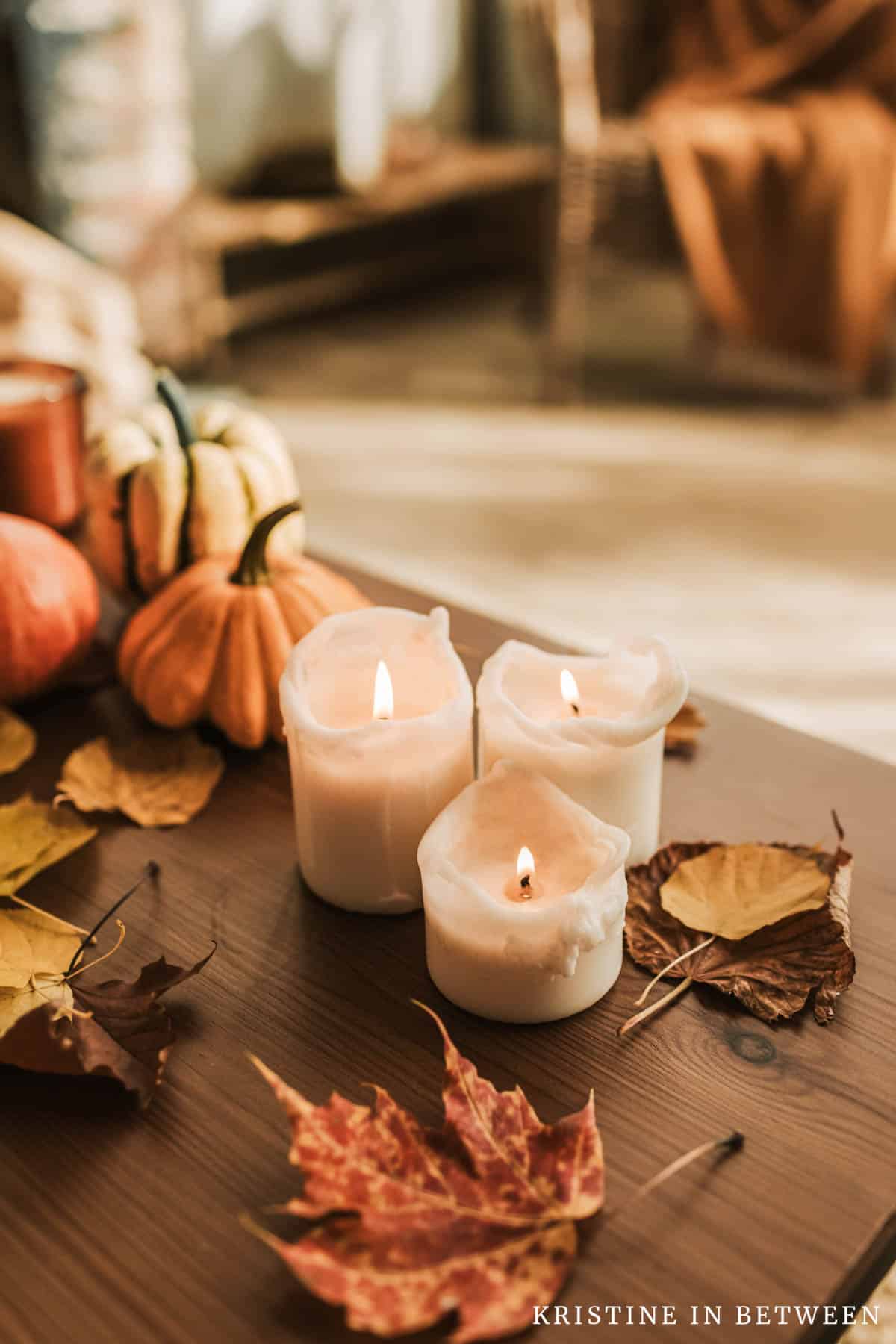 Candles and pumpkins sitting on a coffee table with a chair and an orange blanket in the background.