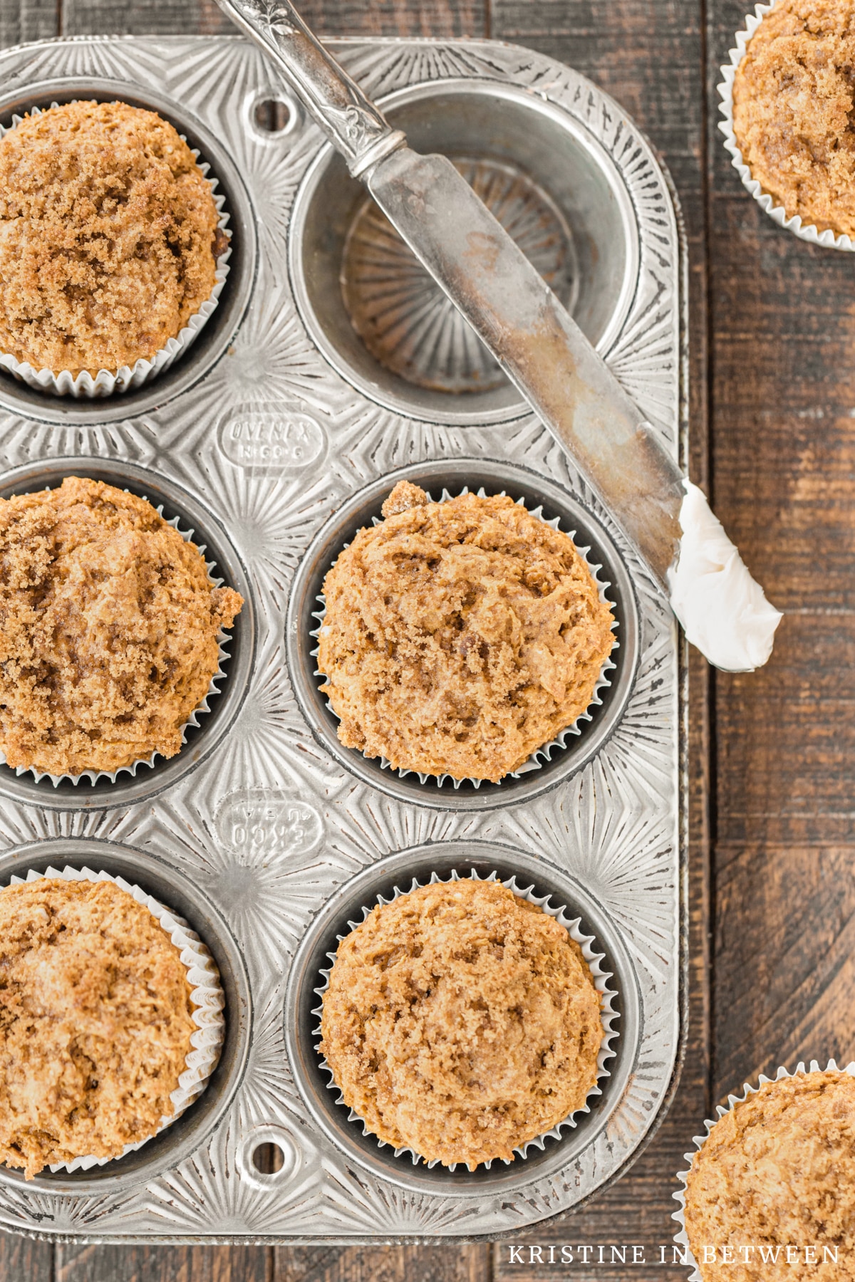 Pumpkin muffins sitting in a muffin tin with a knife and butter.