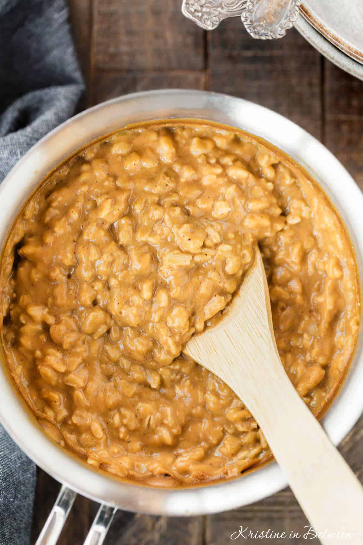 Cooked pumpkin pie oatmeal in a stainless steel pan with a wooden spoon in it.
