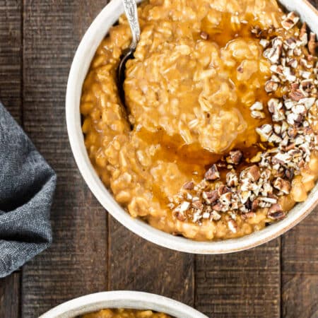A bowl of pumpkin pie oatmeal topped with chopped pecans and a drizzle of maple syrup.