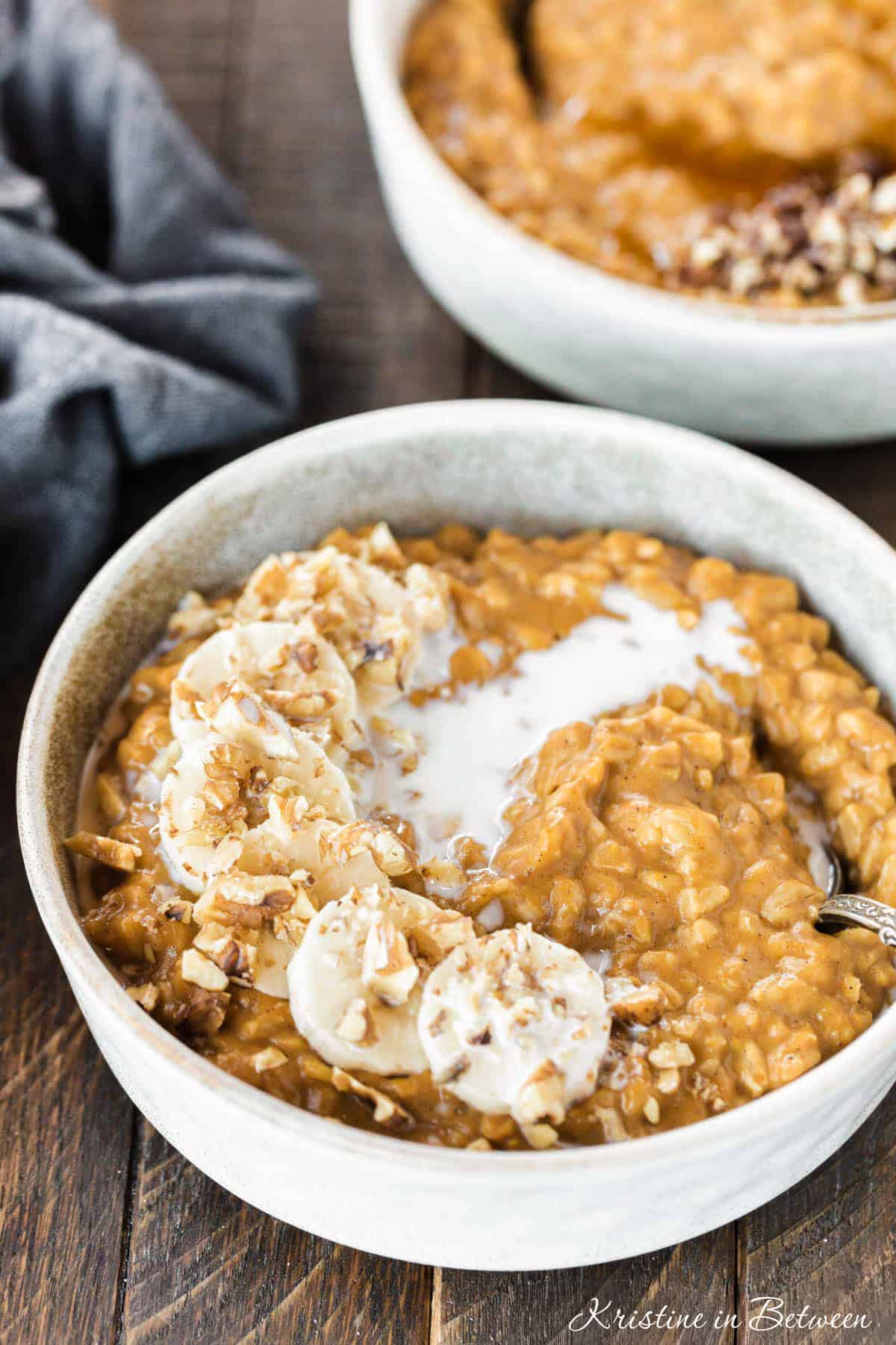 A bowl of pumpkin pie oatmeal topped with bananas and walnuts and a splash of milk.