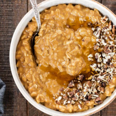 A bowl of pumpkin pie oatmeal topped with chopped pecans and a drizzle of maple syrup.