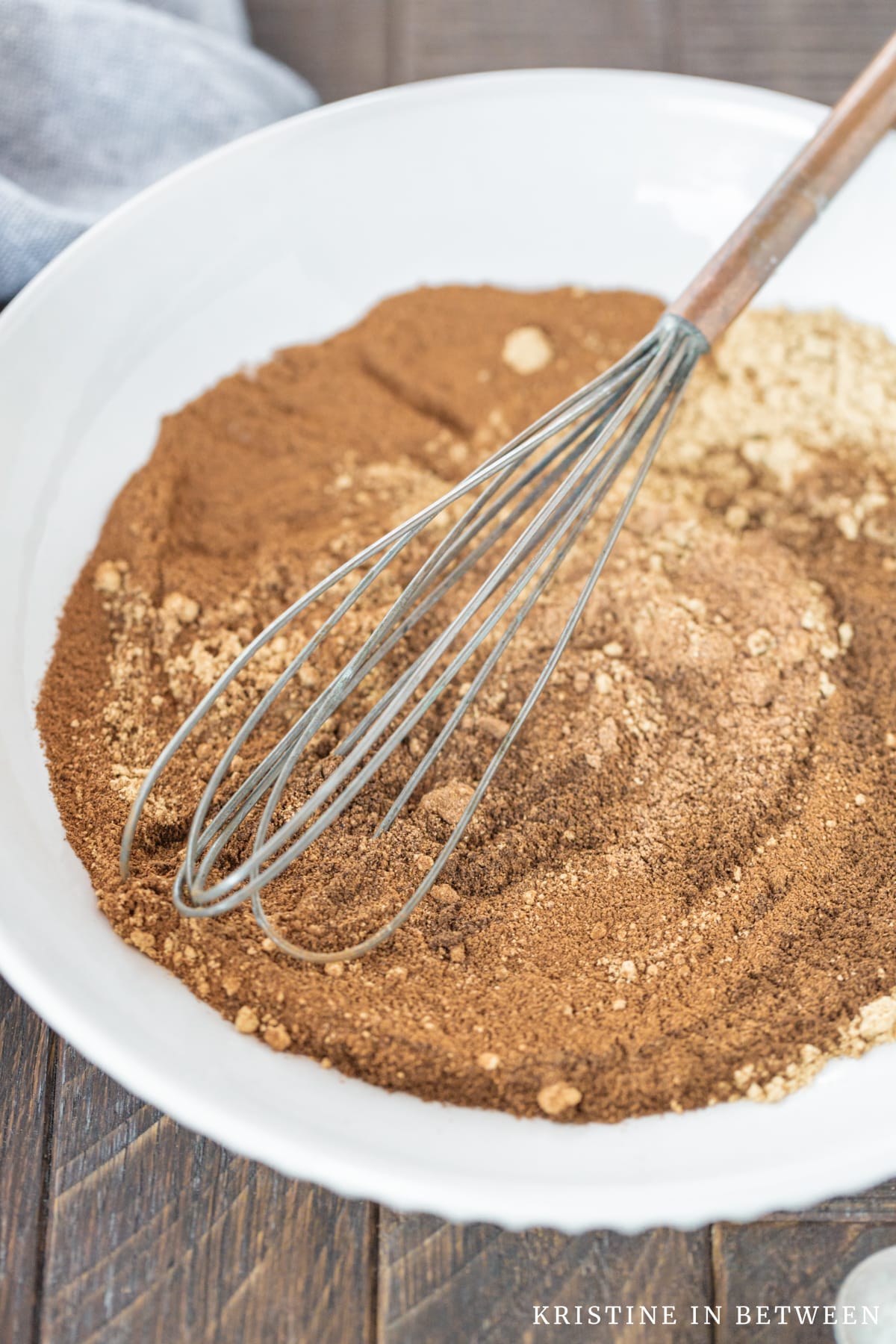 Spices whisked together on a white plate with an old whisk.