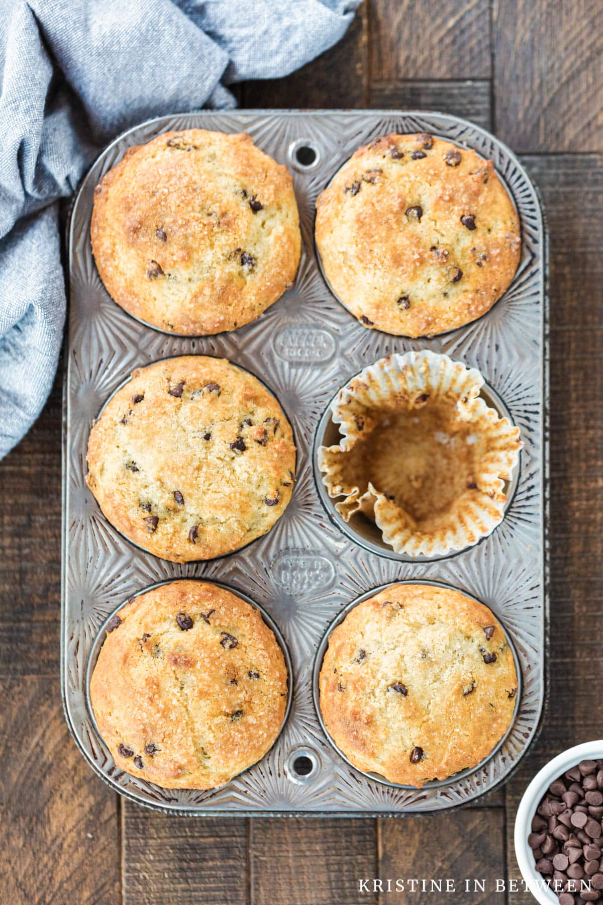 Muffins in a muffin tin with one missing and a light blue napkin sitting next to them.