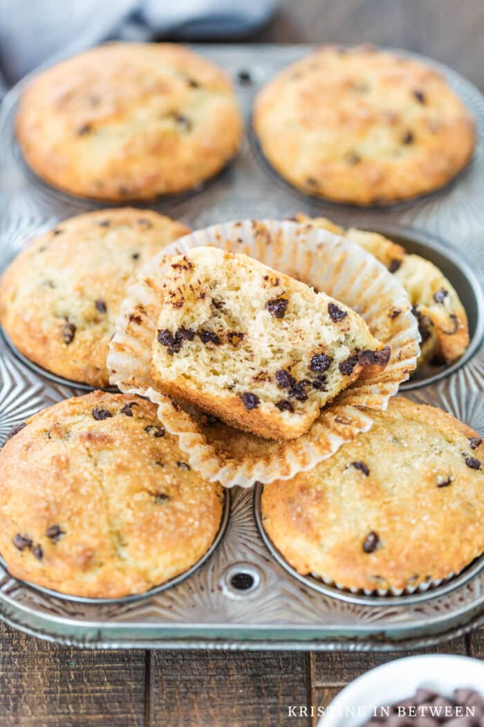 Muffins in a muffin tin with one cut in half on top.