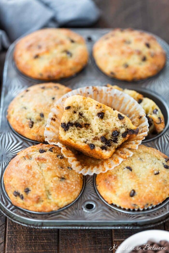Chocolate chip muffins in an antique muffin tin with one broken in half to show the inside.