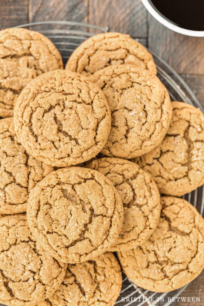 Gingersnap cookies stacked up on a wire rack with a cup of coffee next to them.