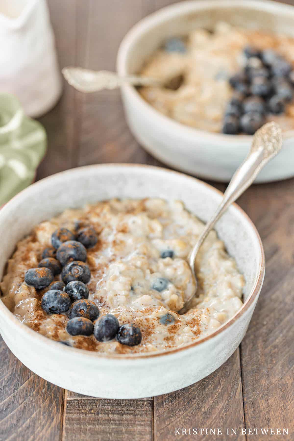 Two bowls of oatmeal topped with blueberries and cinnamon with an orange napkin in the background.