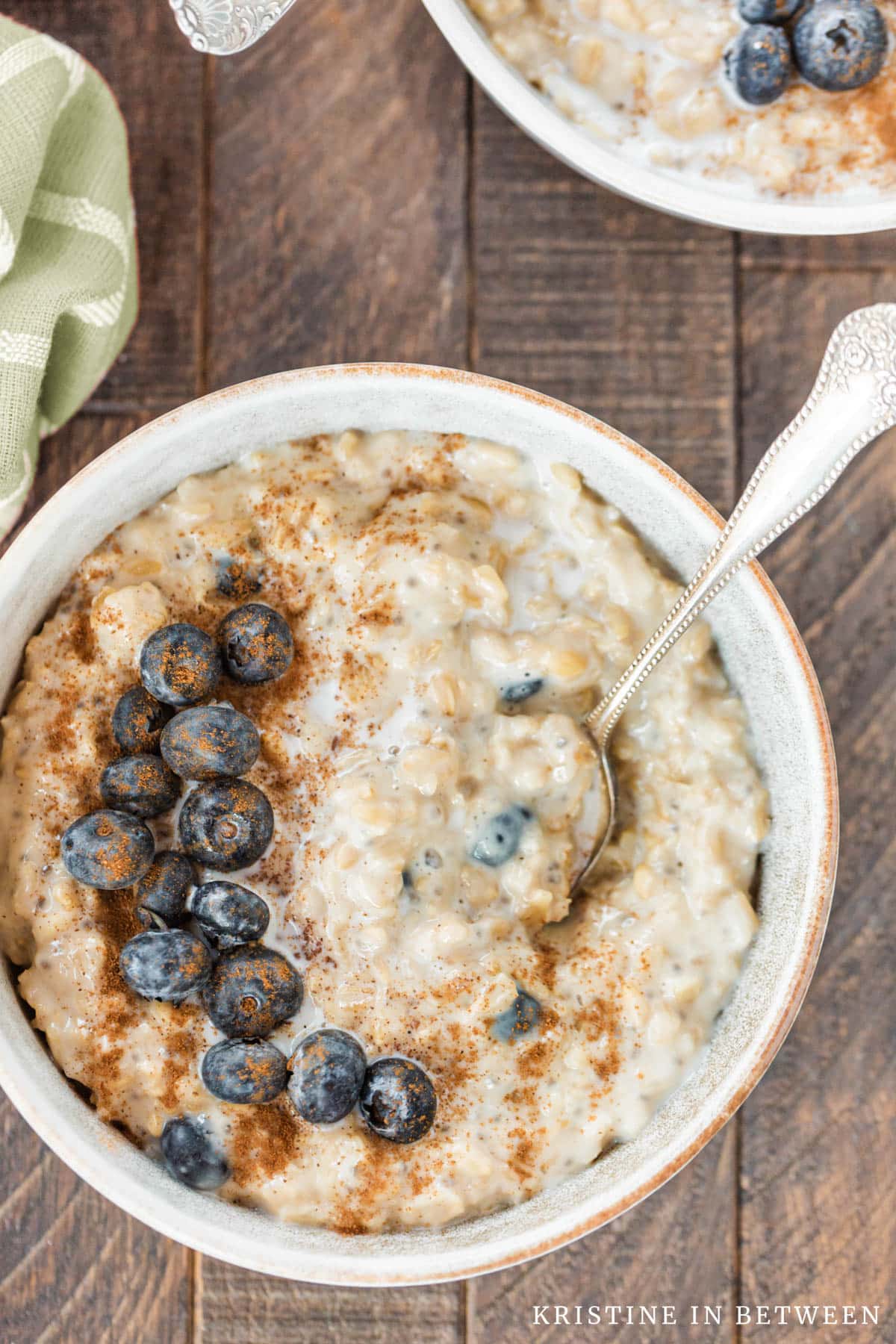 A bowl of oatmeal topped with blueberries and cinnamon with an orange napkin in the background.